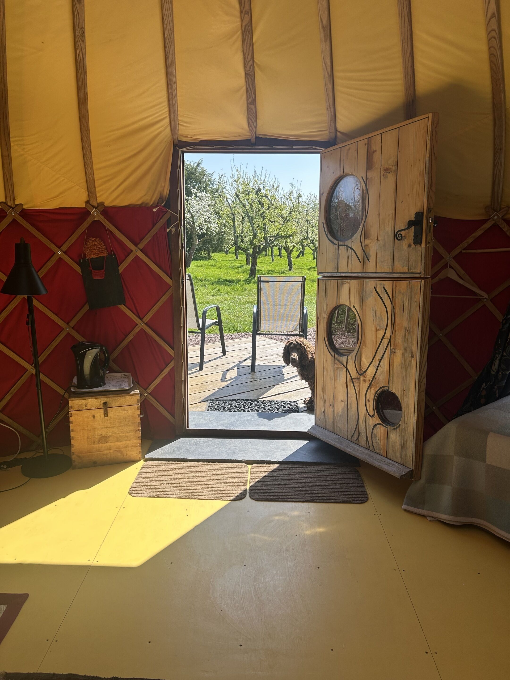 A tent with a wooden interior, a door leading outside, a small table with a kettle, and a chair.