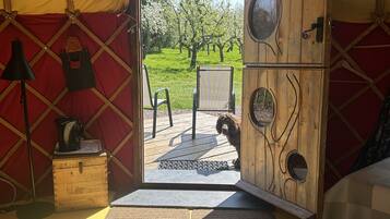 A tent with a wooden interior, a door leading outside, a small table with a kettle, and a chair.