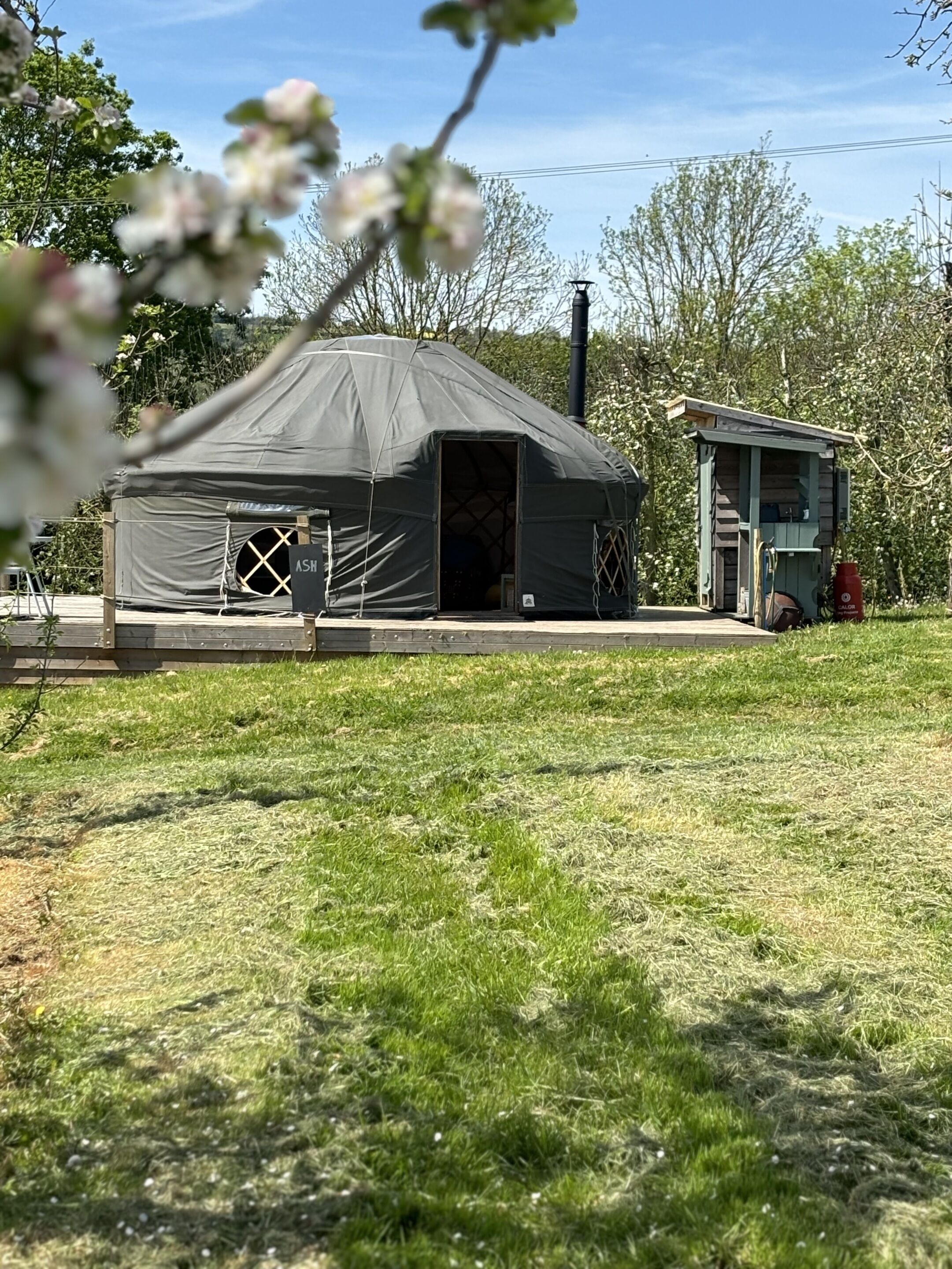 A black tent-like structure with a door, a small shed, and a grassy area in front.