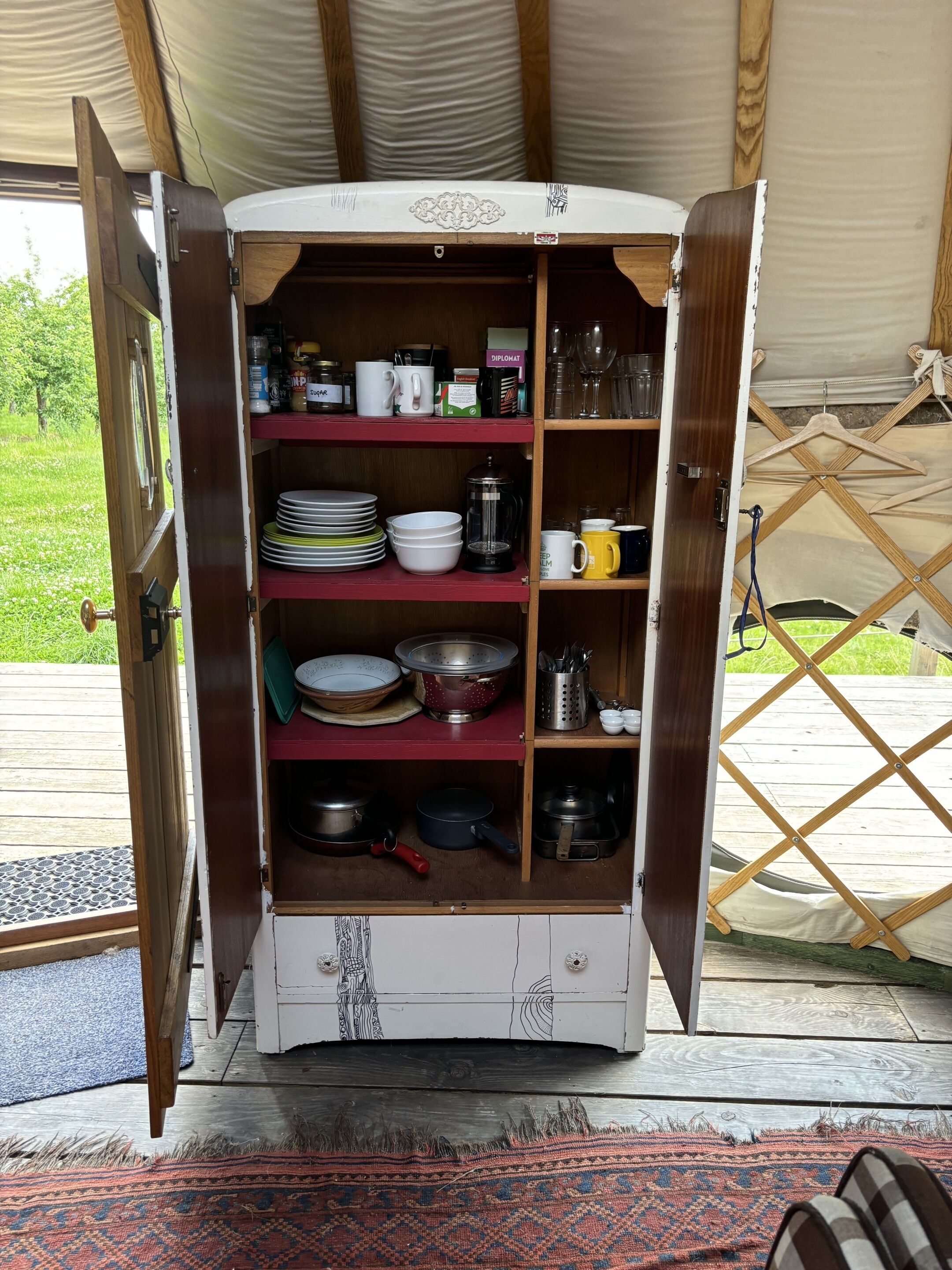 A wooden cabinet with shelves containing kitchenware, plates, and a coffee maker.