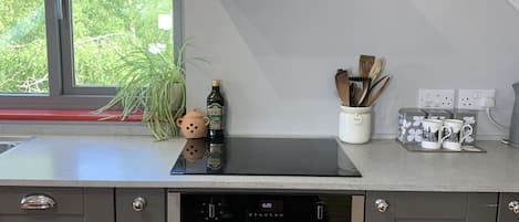 A modern kitchen with grey cabinets, a built-in oven, a stainless steel range hood, and a window with a view of greenery.