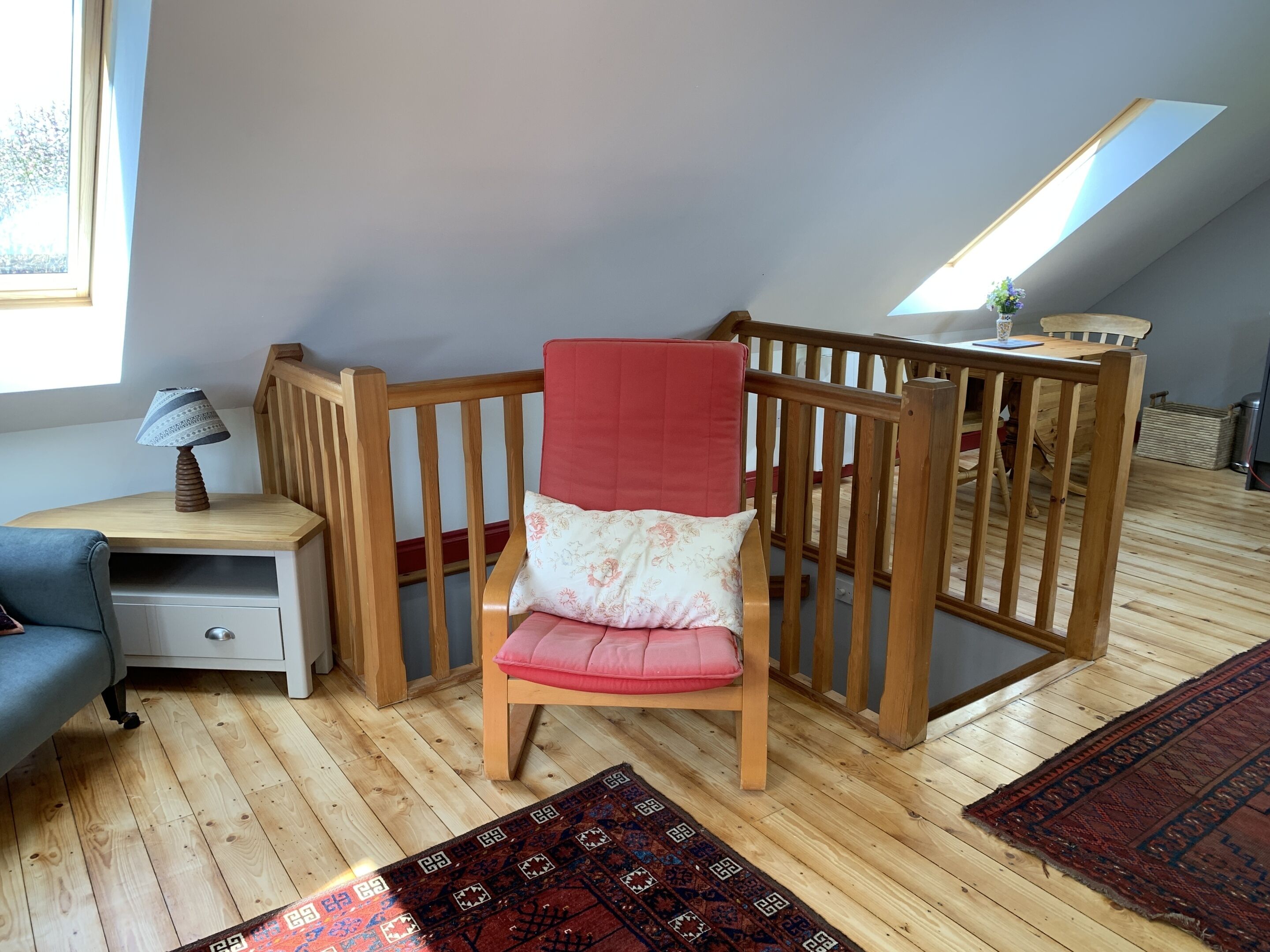 Et hyggeligt rum med en tremmeseng i træ, et lille bord med en lampe, en blå sofa og en tæppe med et mønster.