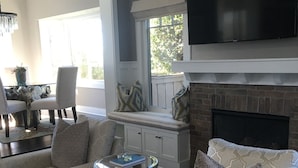 A living room with patterned sofas, a fireplace, a flat-screen TV, and a dining area with a table and chairs.