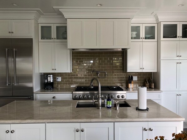 A kitchen with white cabinets, a stainless steel refrigerator, a gas stove, and a tiled backsplash.