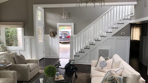 A spacious living room with a staircase, a coffee table with decorative items, and a view of a parked car outside.