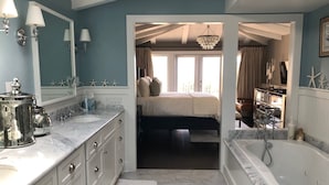 A bathroom with a large bathtub, a sink with a marble countertop, and a mirror with wall sconces.