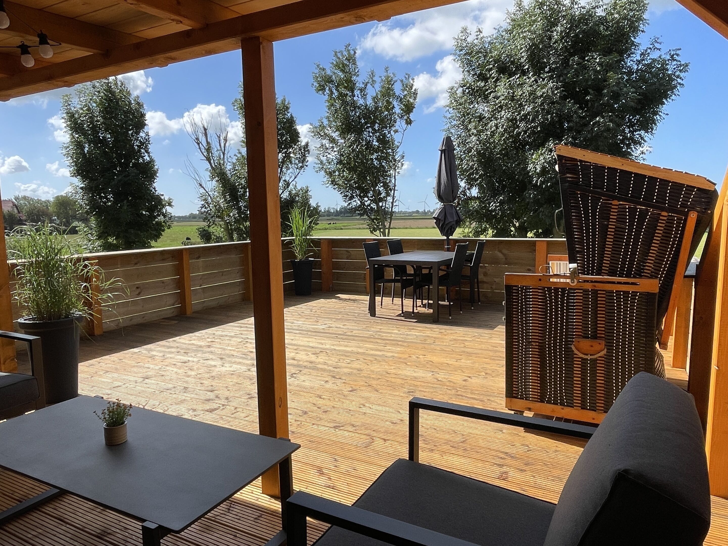 Un patio al aire libre cubierto con suelo de madera, una mesa, sillas y una silla de mimbre.