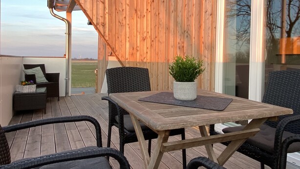 Une terrasse en bois avec une table et des chaises, un pot de fleurs et une vue sur le paysage.