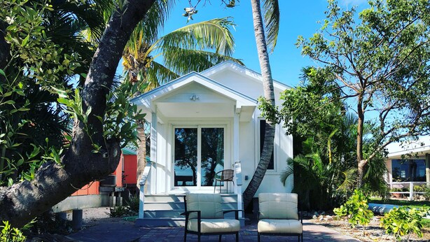 A white building with a covered patio area, surrounded by lush greenery and palm trees. - Paradise on the Bay  (Goodland)