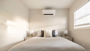 A bedroom with a bed, two bedside tables, a wall-mounted air conditioner, and a window with blinds. - Paradise on the Bay  (Goodland)