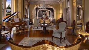 Una sala elegante con un piano de cola, sillones decorados, un candelabro y una chimenea.