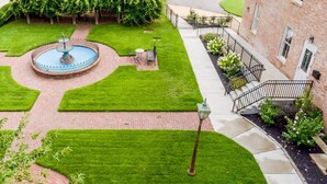 Un patio con una fuente, césped bien cuidado y un edificio de ladrillo.
