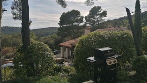 A patio area with a grill, surrounded by trees and a view of a hillside.