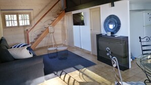 A modern living room with a wooden staircase, a sofa, a coffee table, a TV, and a decorative mirror.