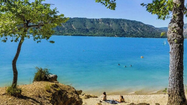 A lake with clear blue water, surrounded by trees and hills.