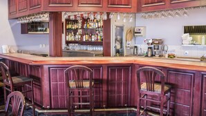 A bar area with wooden cabinets, a counter, and bar stools. There are shelves with bottles and glasses behind the counter. - Ramada by Wyndham Nisku (Nisku)