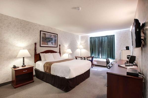 A hotel room with a large bed, bedside tables with lamps, a desk with a computer, a chair, and a window with curtains. - Ramada by Wyndham Nisku (Nisku)