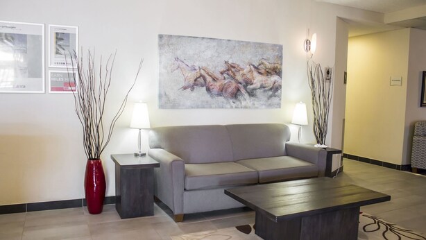 A modern lobby with a grey sofa, two side tables with lamps, a coffee table, and a painting of horses. - Ramada by Wyndham Nisku (Nisku)