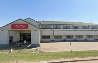 Un edificio con un letrero que dice "RAMADA BY WYNDHAM" y un estacionamiento al frente.