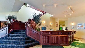 A hotel lobby with a staircase, a reception desk, and a wall sign reading "Quality & Suites". - Ramada by Wyndham Nisku (Nisku)
