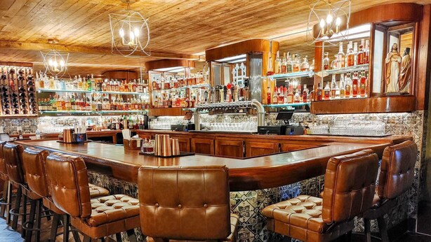 Eine Bar mit Holzbalkendecke, Lederbarkreuzern und Regalen voller Spirituosenflaschen.