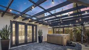 Eine überdachte Terrasse mit Whirlpool, Blumentöpfen und Lichterketten.