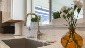 Eine moderne Küche mit Spüle aus Edelstahl, einer Marmorarbeitsplatte und einer Vase mit weißen Blumen.