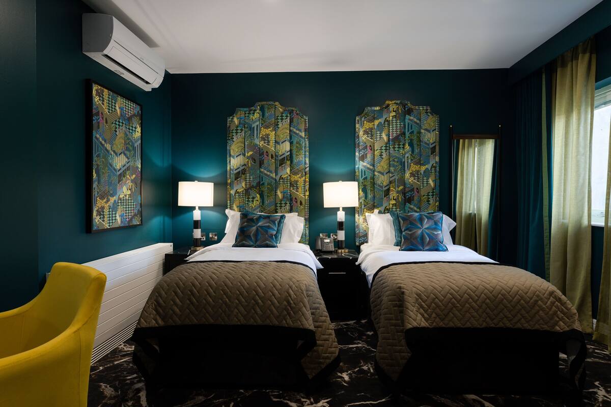 A hotel room with two beds, a yellow armchair, and artwork on the walls.