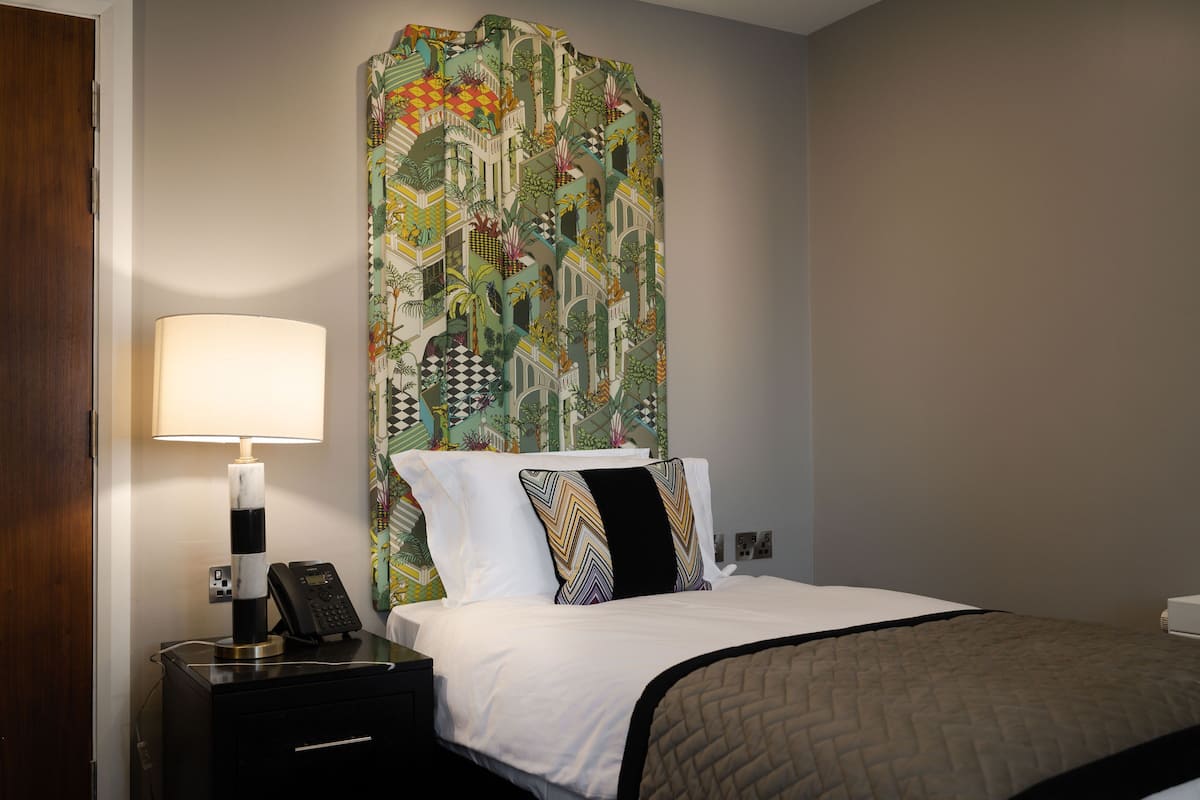 A hotel room with a bed, a nightstand with a lamp, and a telephone.