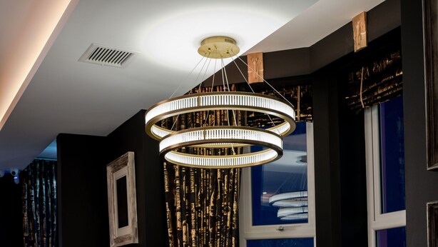 A dining area with a chandelier, patterned chairs, and a view of the city at night. - Elephant Rock Hotel (Portrush)