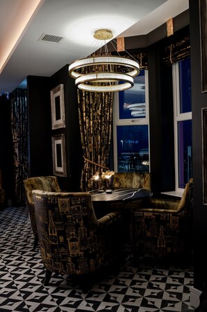 A dining area with a chandelier, patterned chairs, and a view of the city at night. - Elephant Rock Hotel (Portrush)
