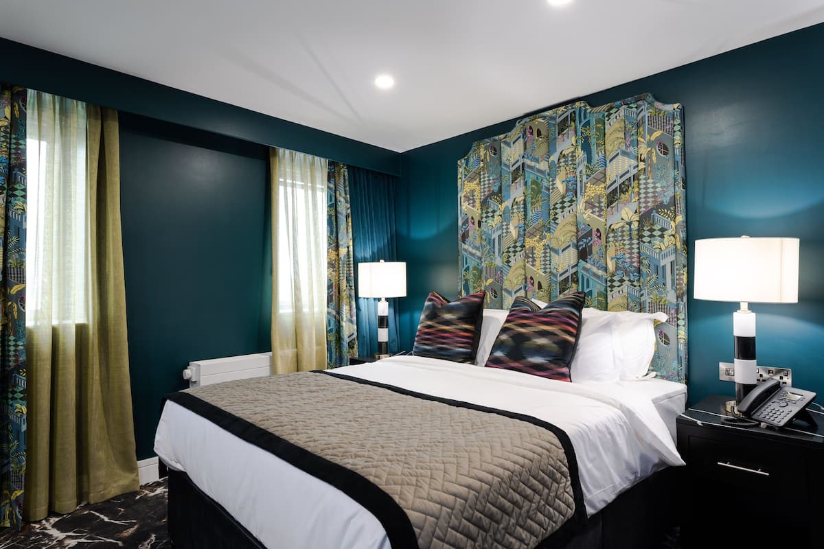A hotel room with a large bed, two bedside lamps, a telephone, and a patterned wall.