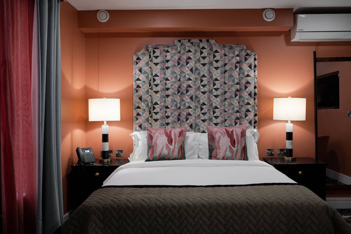A hotel room with a bed, two bedside tables, a telephone, and a wall-mounted air conditioner.