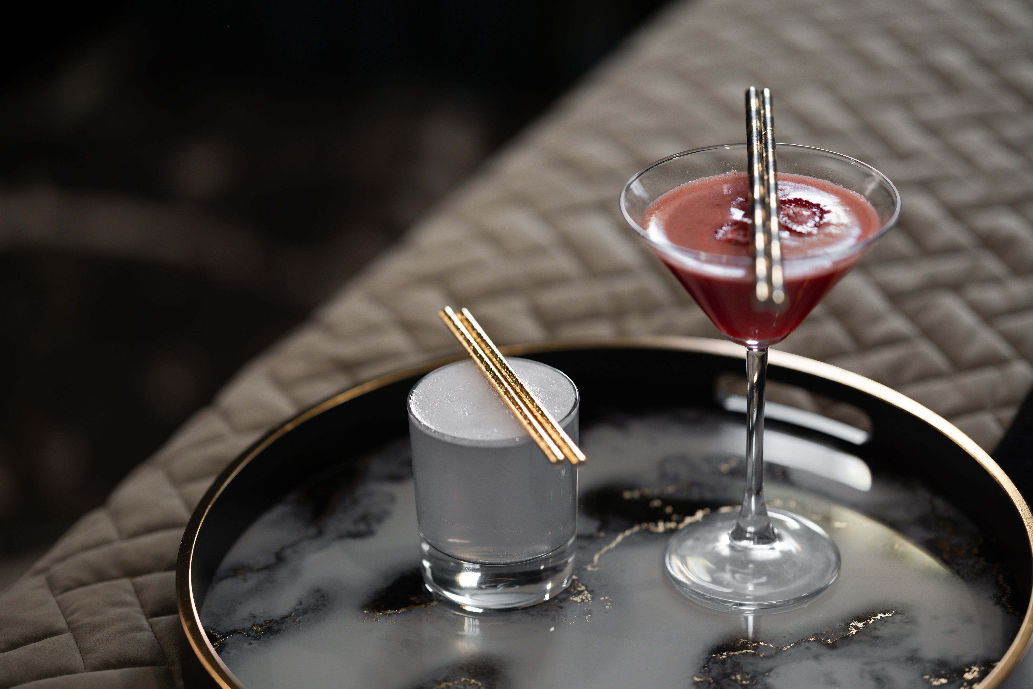 Two drinks on a tray, one in a martini glass and one in a shot glass, with a gold-colored spoon resting on the shot glass.