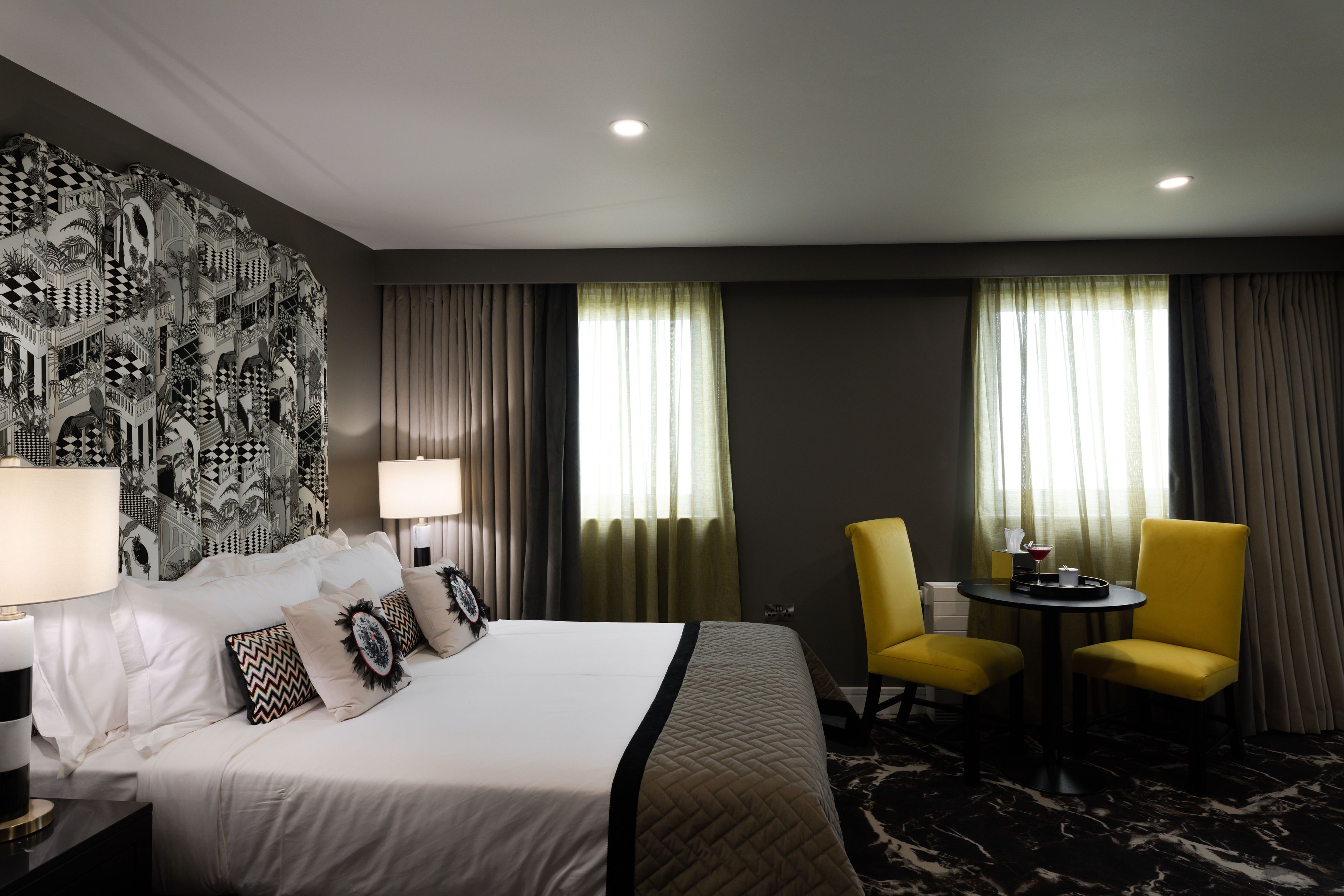 Habitación de hotel con una cama grande, dos sillas, una mesita pequeña y un tapiz decorativo en la pared.