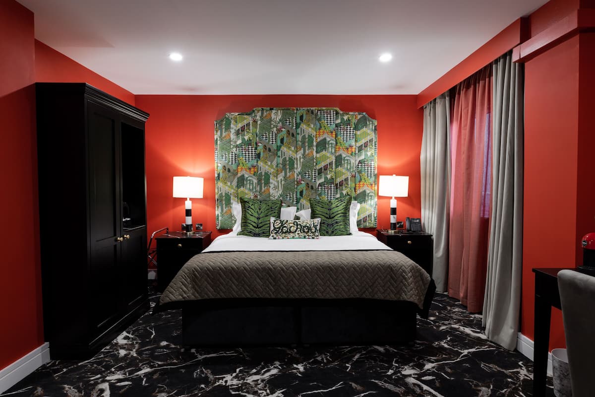 A hotel room with a large bed, two bedside tables, a wardrobe, and a headboard with a colorful pattern.