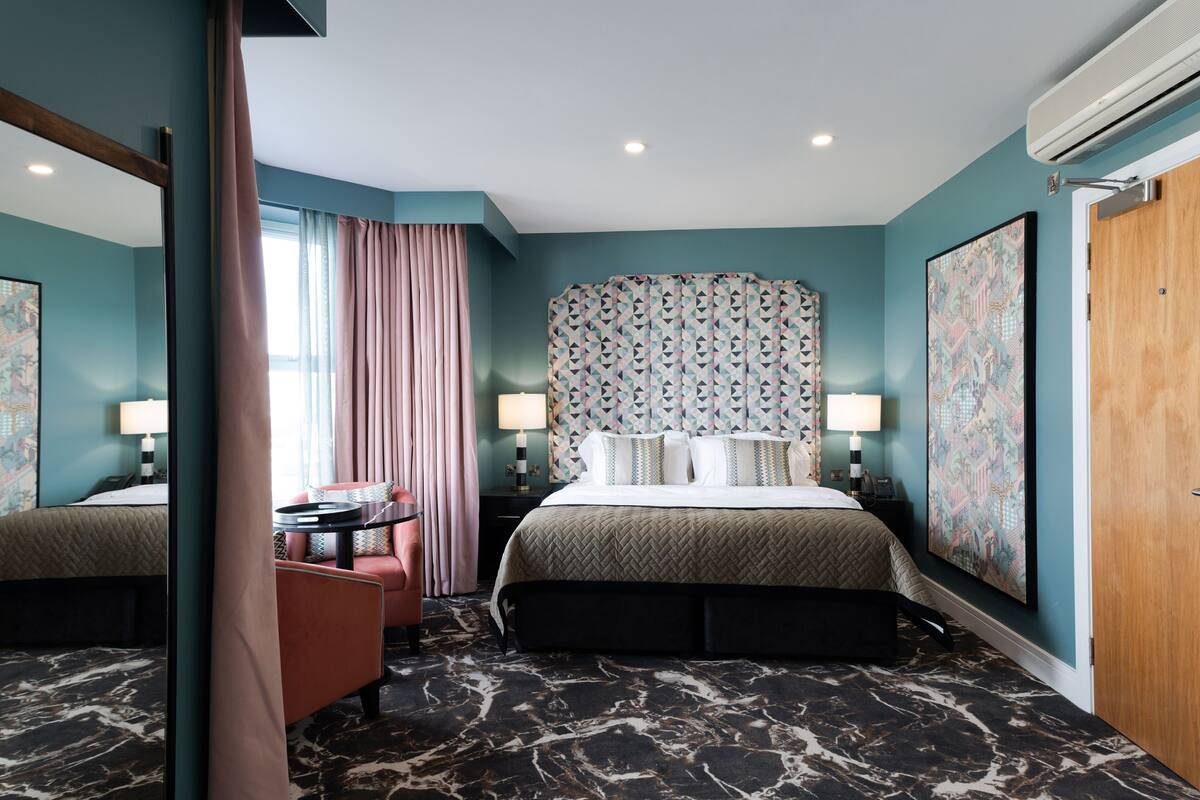 A hotel room with a bed, a desk, a chair, and a large window with curtains.