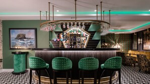 A bar area with a counter, green upholstered bar stools, a wine rack, and a framed picture on the wall. - Elephant Rock Hotel (Portrush)