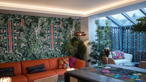 A modern living room with a tropical-themed wallpaper, a red sofa, and a dining area with a glass top table. - Elephant Rock Hotel (Portrush)