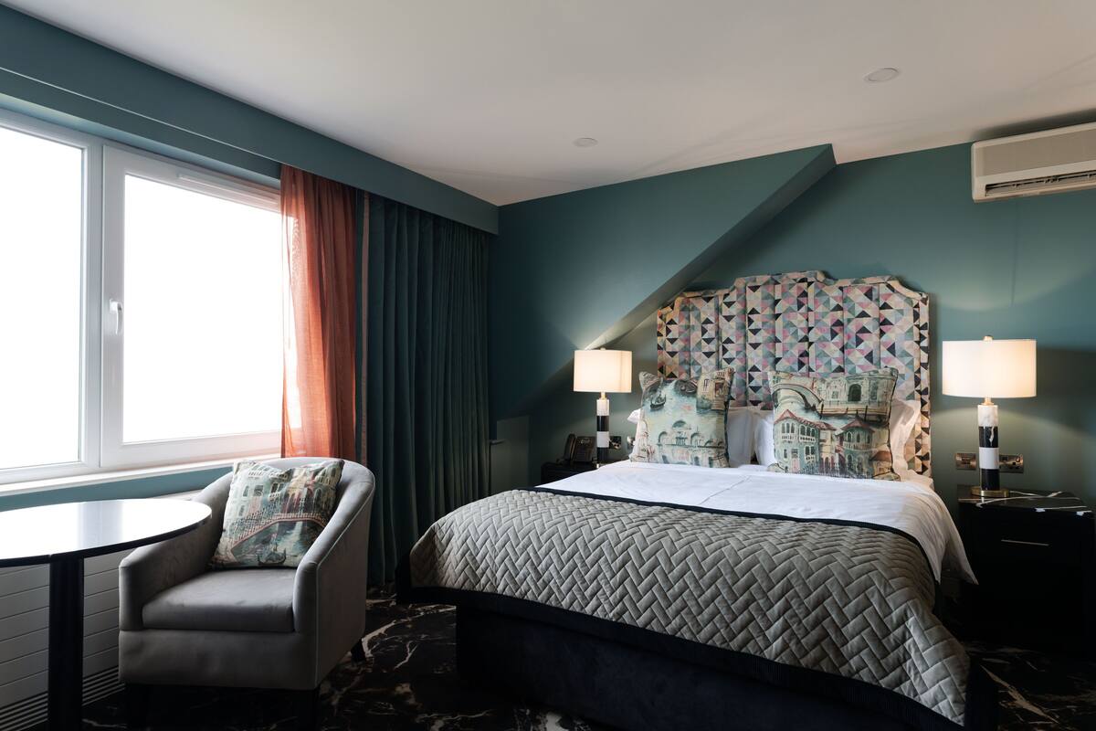 A hotel room with a bed, a chair, a table, and a window with curtains.