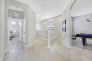 A spacious hallway with a pool table, a staircase, and a door leading to a bedroom.