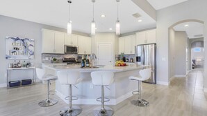 Una cocina moderna con armarios blancos, electrodomésticos de acero inoxidable y una isla central con taburetes de bar.