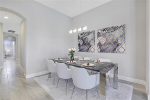 Un espace repas avec une table rectangulaire, des chaises blanches et deux tableaux abstraits accrochés au mur.