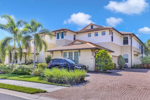 A two-story house with a driveway, palm trees, and a car parked in front.