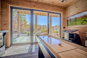 Ein Zimmer mit Schreibtischfußball, Billardtisch und einem großen Fenster mit Blick auf Bäume und Hügel.