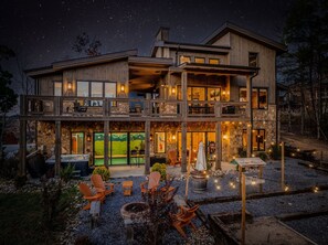 Une maison en bois à deux étages, dotée d’une façade en pierre, d’un espace extérieur aménagé pour s’asseoir et d’un foyer.