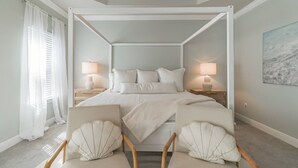Uma cama de dossel com lençóis brancos, duas mesas de cabeceira com abajures e um quadro na parede.