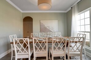 A dining area with a wooden table and white chairs, a painting on the wall, and a window with curtains. - 30A! Minutes to Beach! Best Pool Access! Games (Santa Rosa Beach)