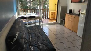 Ein Balkon mit einer Couch, einem Tisch und Stühlen. Ein Fernseher ist an der Wand befestigt und es gibt ein Sideboard mit einem Kühlschrank.