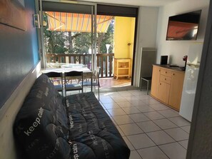 Un balcón con un sofá, una mesa y sillas. Hay un televisor montado en la pared y un mueble con refrigerador.